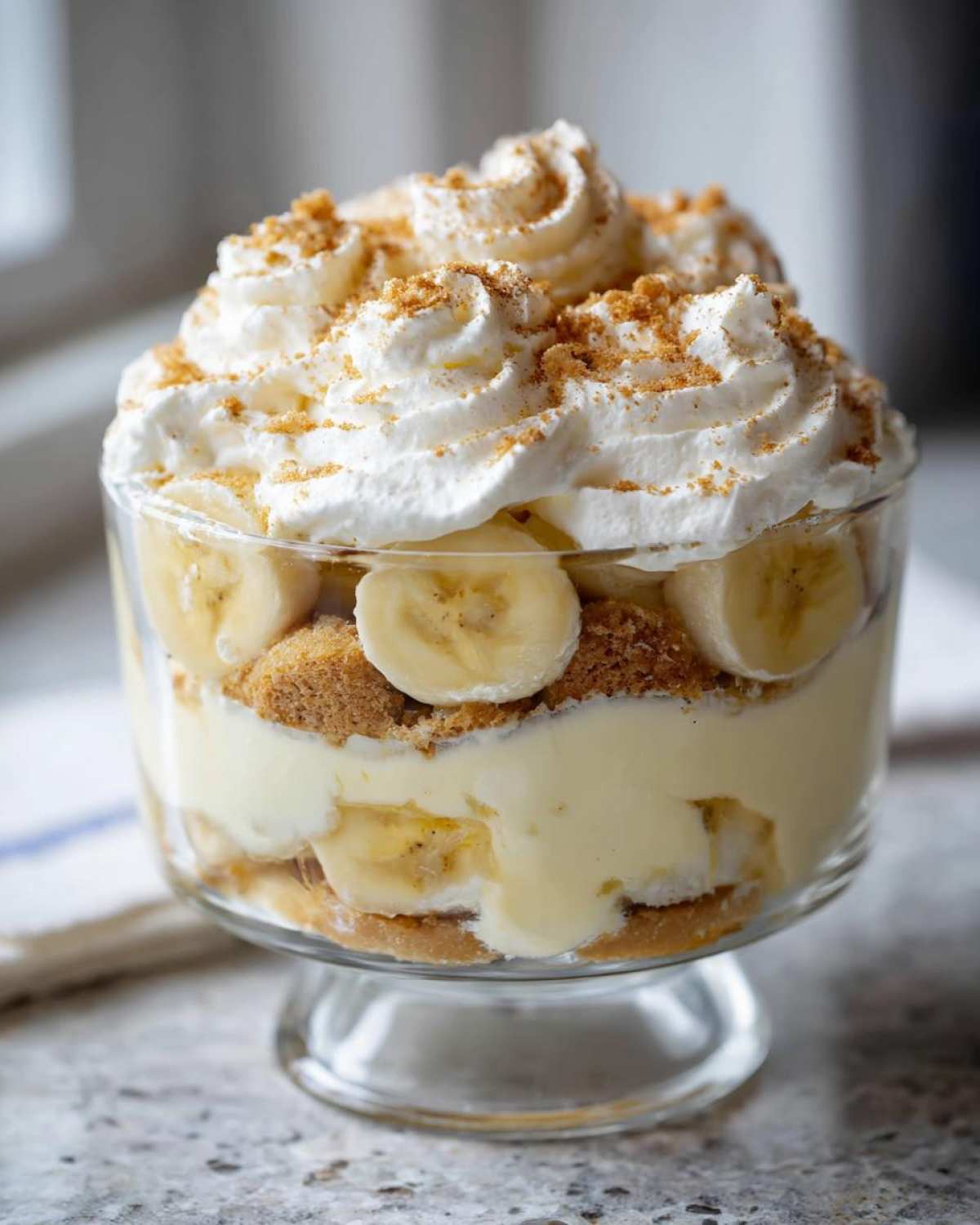 Close-up of a layered single-serving banana pudding in a glass dish, topped with whipped cream.