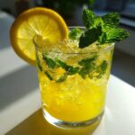 A close-up of a Sparkling Lemon Mint Mocktail filled with crushed ice, mint leaves, and garnished with a lemon wheel.