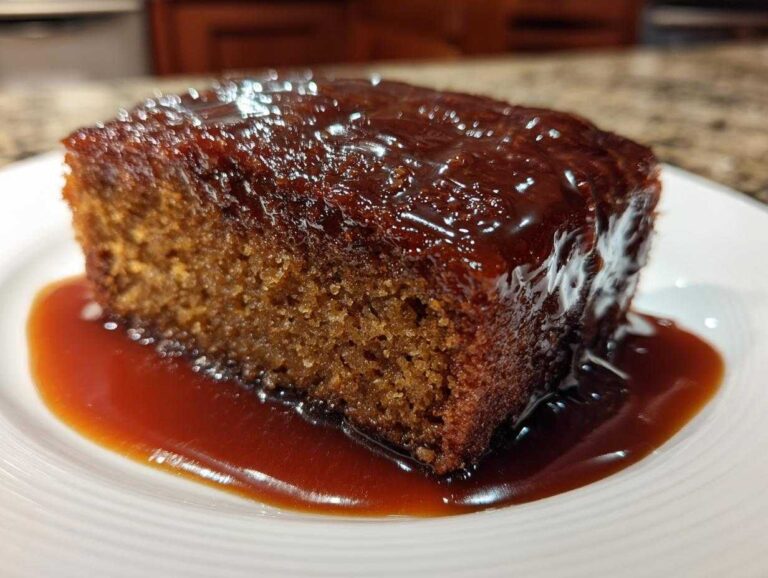 A close-up of a square slice of moist sticky toffee pudding recipe smothered in rich toffee sauce.