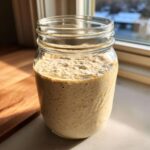 A glass jar filled with active, bubbly sourdough starter, showing significant rise and texture.