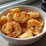 Close-up of seasoned, cooked air fryer frozen shrimp piled high in a small white bowl.