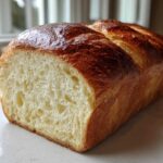 A freshly baked loaf of soft milk bread, sliced to show the fluffy interior and golden brown, shiny crust.
