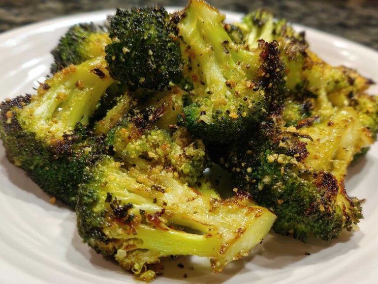Close-up of beautifully seasoned and charred roasted broccoli florets piled on a white plate.