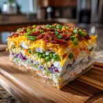 A thick, perfectly layered slice of amazing 7 layer salad topped with cheese, bacon, and green onions.