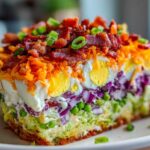 Close-up of a perfectly layered slice of 7 layer salad showing distinct layers of vegetables, eggs, cheese, and bacon.