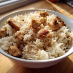 Close-up of perfectly cooked chicken and rice mixture served in a white bowl.