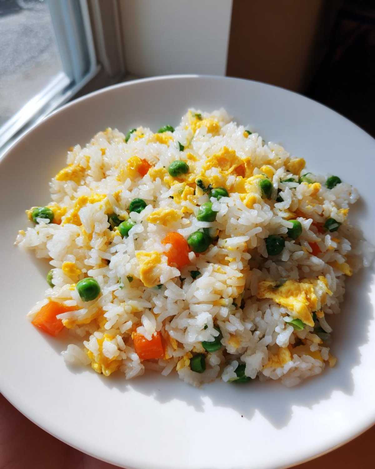A serving of bright and fluffy Egg Fried Rice mixed with scrambled egg pieces, green peas, and diced carrots on a white plate.