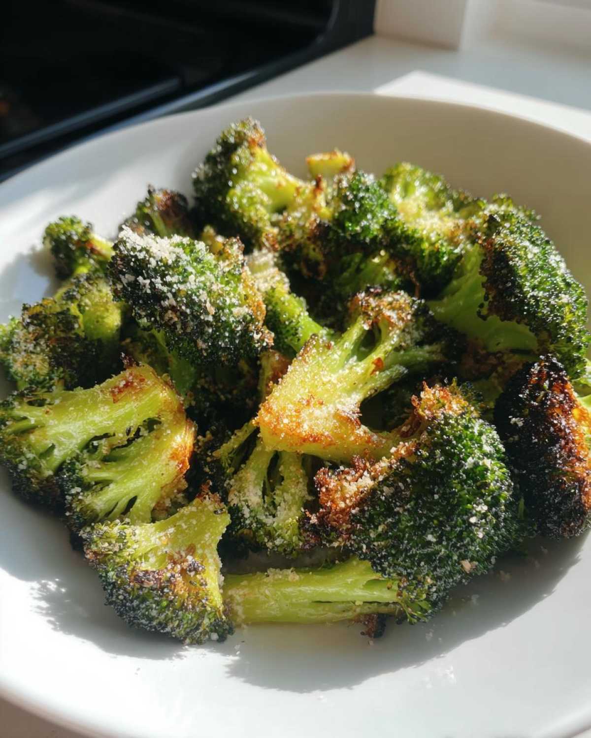 Close-up of vibrant green roasted broccoli florets topped with grated Parmesan cheese in a white bowl.