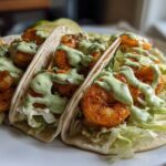 Three soft tortilla Shrimp Tacos filled with seasoned shrimp, shredded lettuce, and drizzled generously with a creamy green sauce.