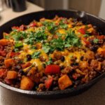 Close-up of a savory sweet potato skillet with ground meat, black beans, melted cheese, and fresh cilantro.