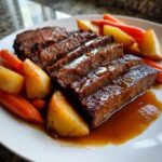 Close-up of sliced Apple Cider Braised Brisket covered in rich gravy, served with roasted carrots and potatoes.