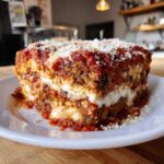 A thick, layered slice of Authentic Eggplant Parmesan Recipe covered in rich tomato sauce and grated cheese.