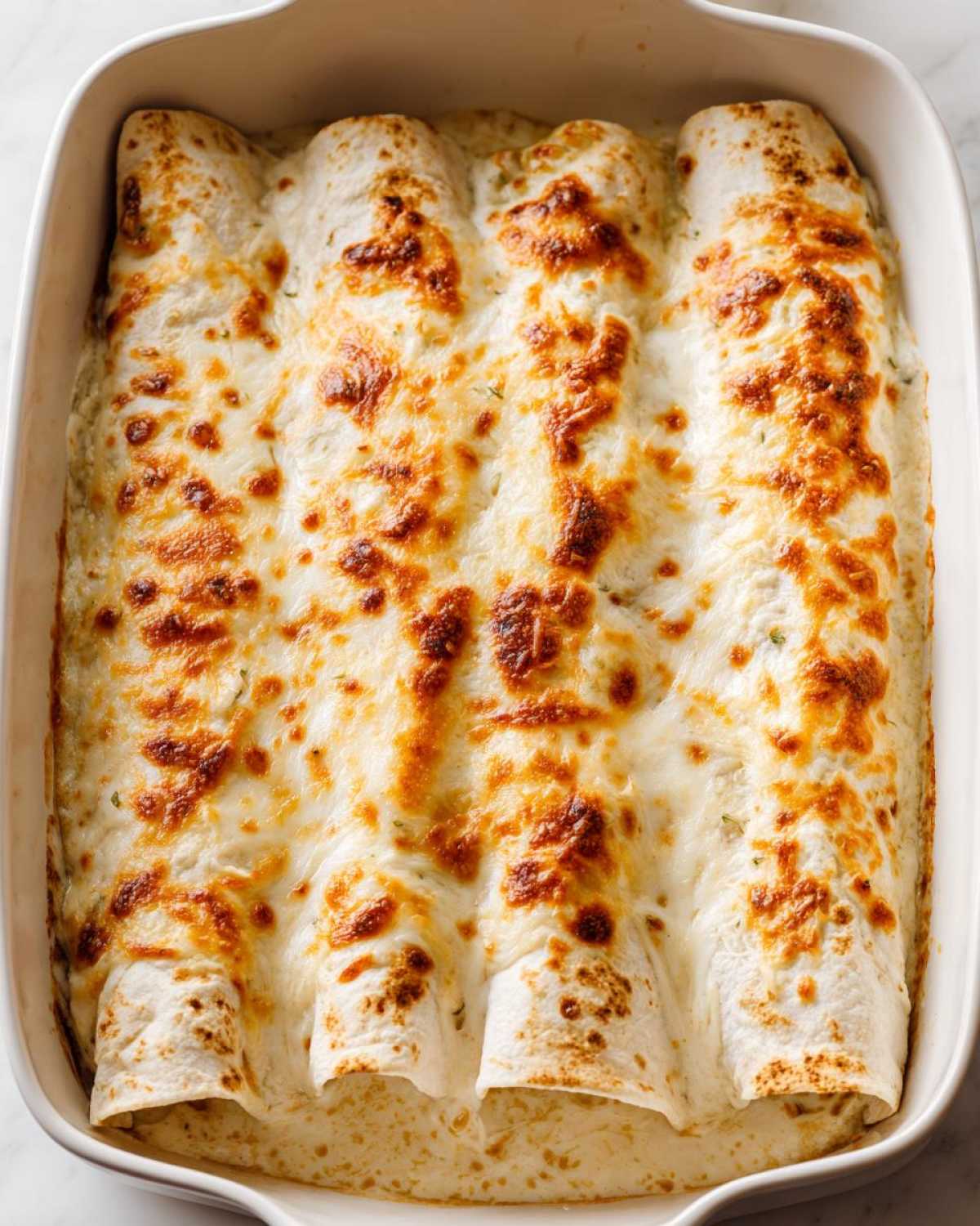 Close-up overhead view of baked white chicken enchiladas covered in melted, bubbly, and slightly browned cheese sauce.