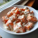Close-up of orange, cubed Bang Bang Salmon Bites generously coated in a creamy white sauce and sprinkled with herbs.