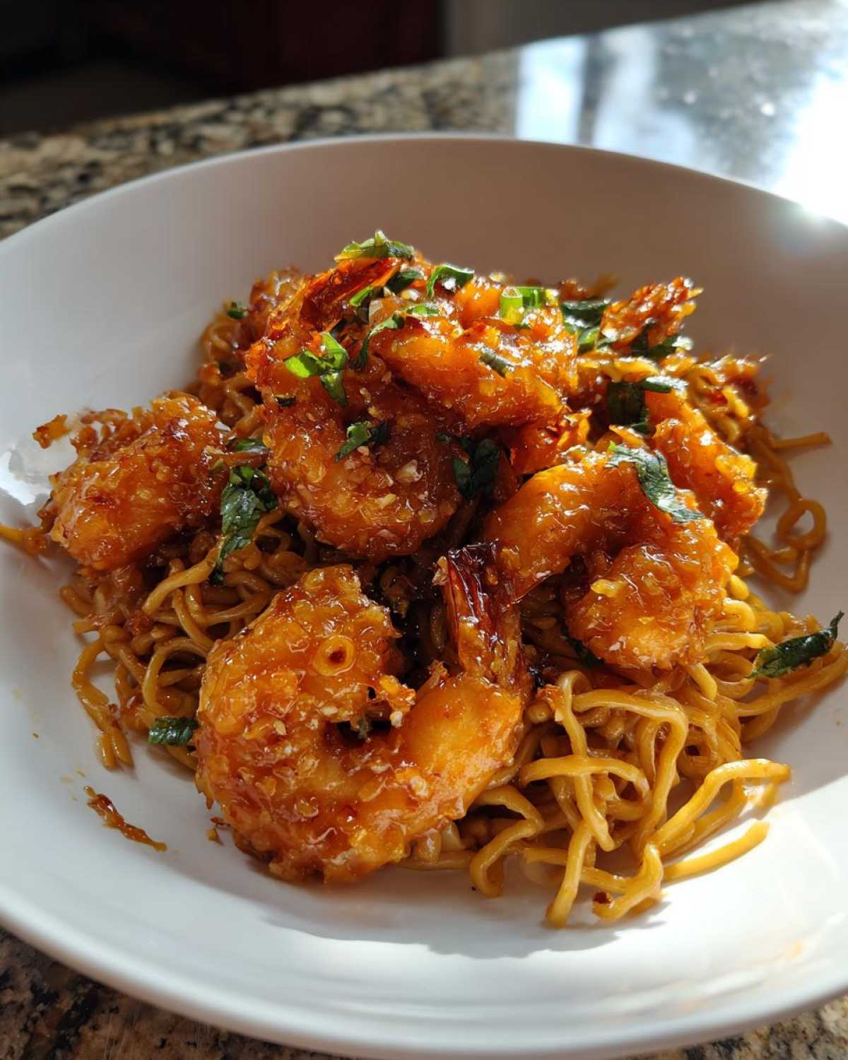 Close-up of crispy, saucy Bang Bang Shrimp Noodle served in a white bowl, garnished with green herbs.