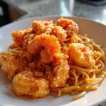 A close-up of crispy Bang Bang Shrimp served over creamy noodles in a white bowl.