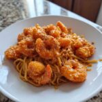 A white plate piled high with saucy noodles topped generously with crispy, orange Bang Bang Shrimp Noodle.
