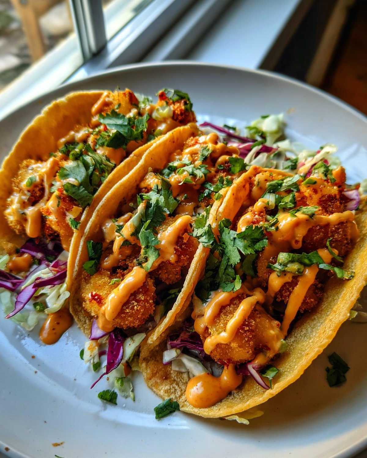 Three delicious Bang Bang Shrimp Tacos filled with crispy shrimp, slaw, and drizzled with spicy sauce and cilantro.