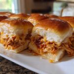 Close-up of several glossy, baked bbq chicken sliders filled with shredded chicken and melted cheese on a white serving dish.