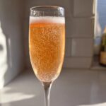 A close-up of a sparkling, orange-hued bellini recipe cocktail in a champagne flute, catching the sunlight.