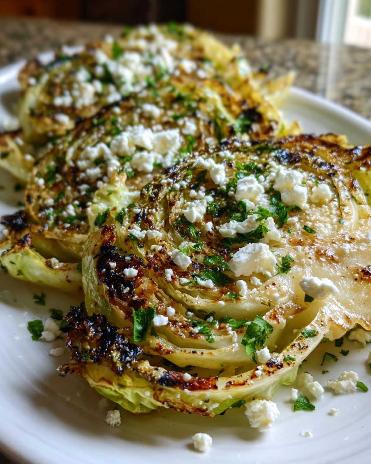 Close-up of several Blistered Cabbage Steaks with Feta cheese crumbles and fresh parsley on a white plate.