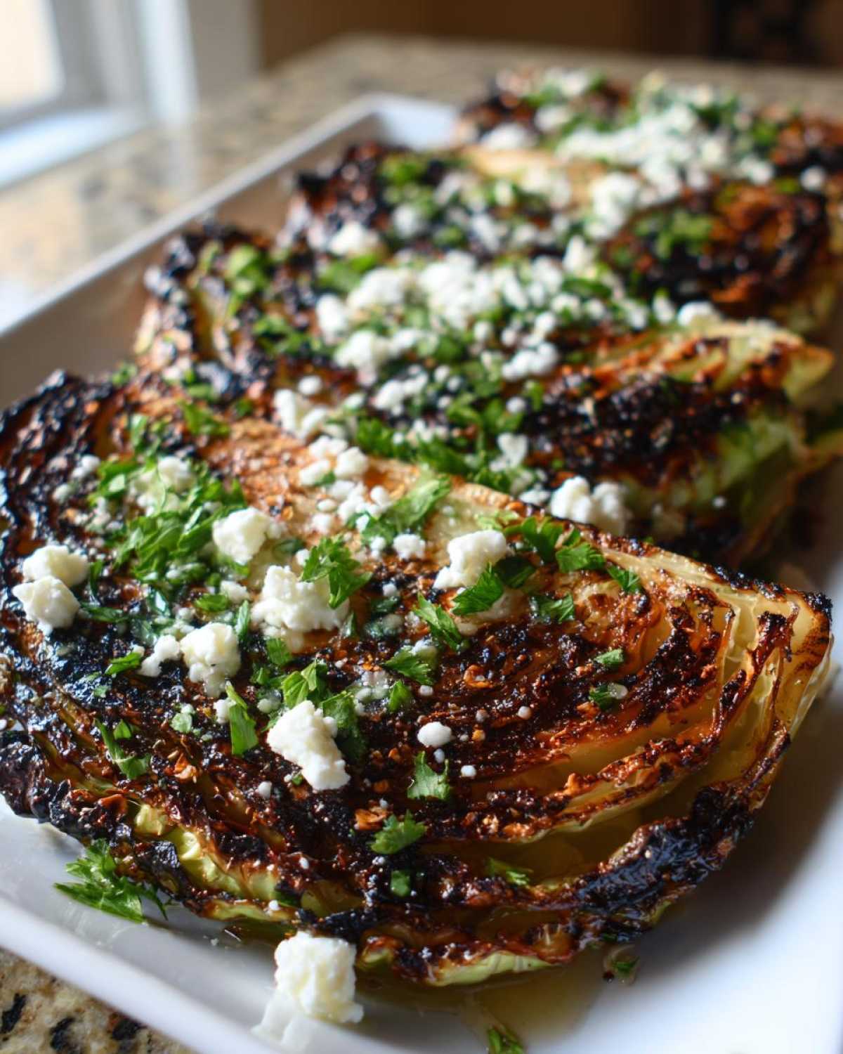 Close-up of perfectly cooked Blistered Cabbage Steaks with Feta cheese crumbles and fresh chopped parsley.