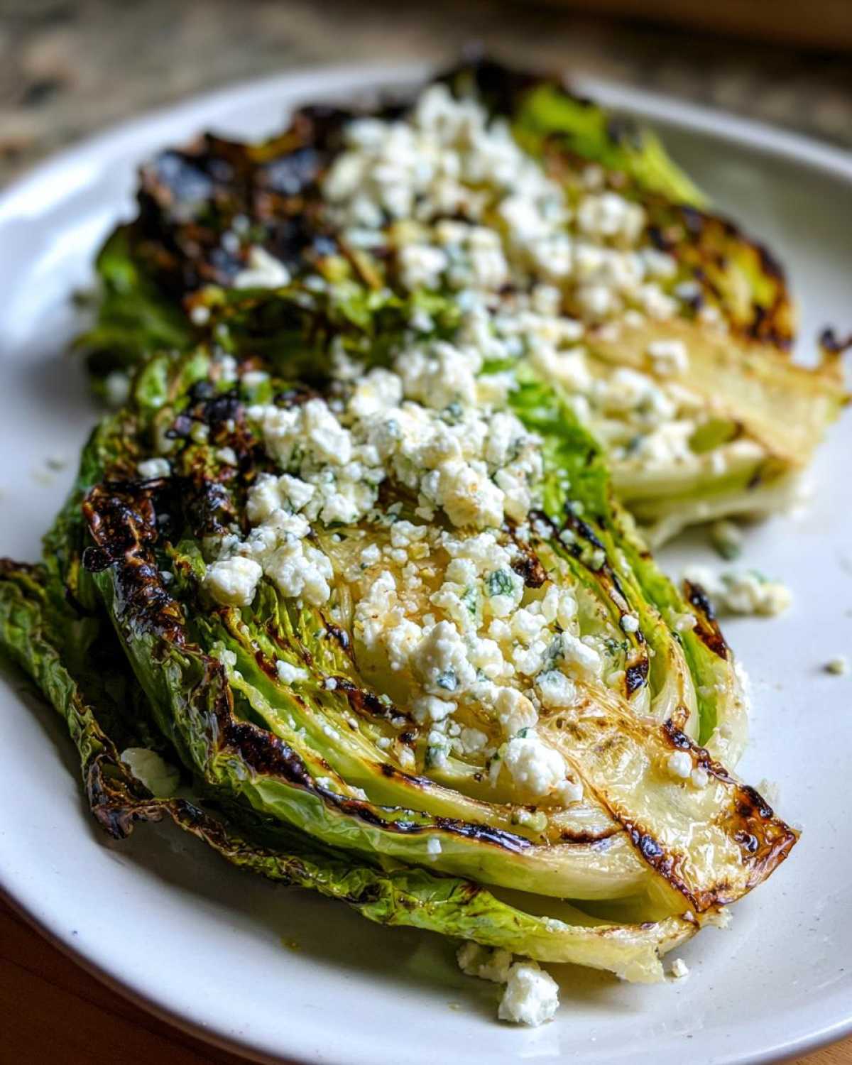Two halves of Blistered Cabbage Steaks topped generously with crumbled feta cheese on a white plate.