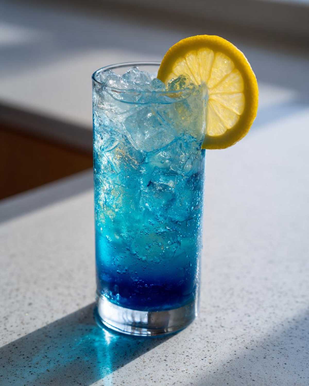 A tall glass filled with a vibrant Blue Drinks Aesthetic Cocktail, ice, and garnished with a bright lemon slice.