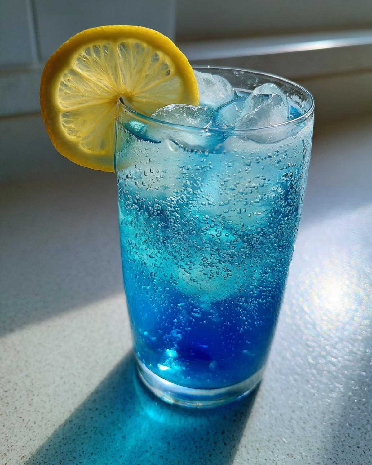 Close-up of a vibrant Blue Drinks Aesthetic Cocktail filled with ice and garnished with a bright lemon slice.