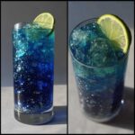 A tall glass holding a shimmering, layered Blue Drinks Aesthetic Mocktail with ice and a fresh lime slice.