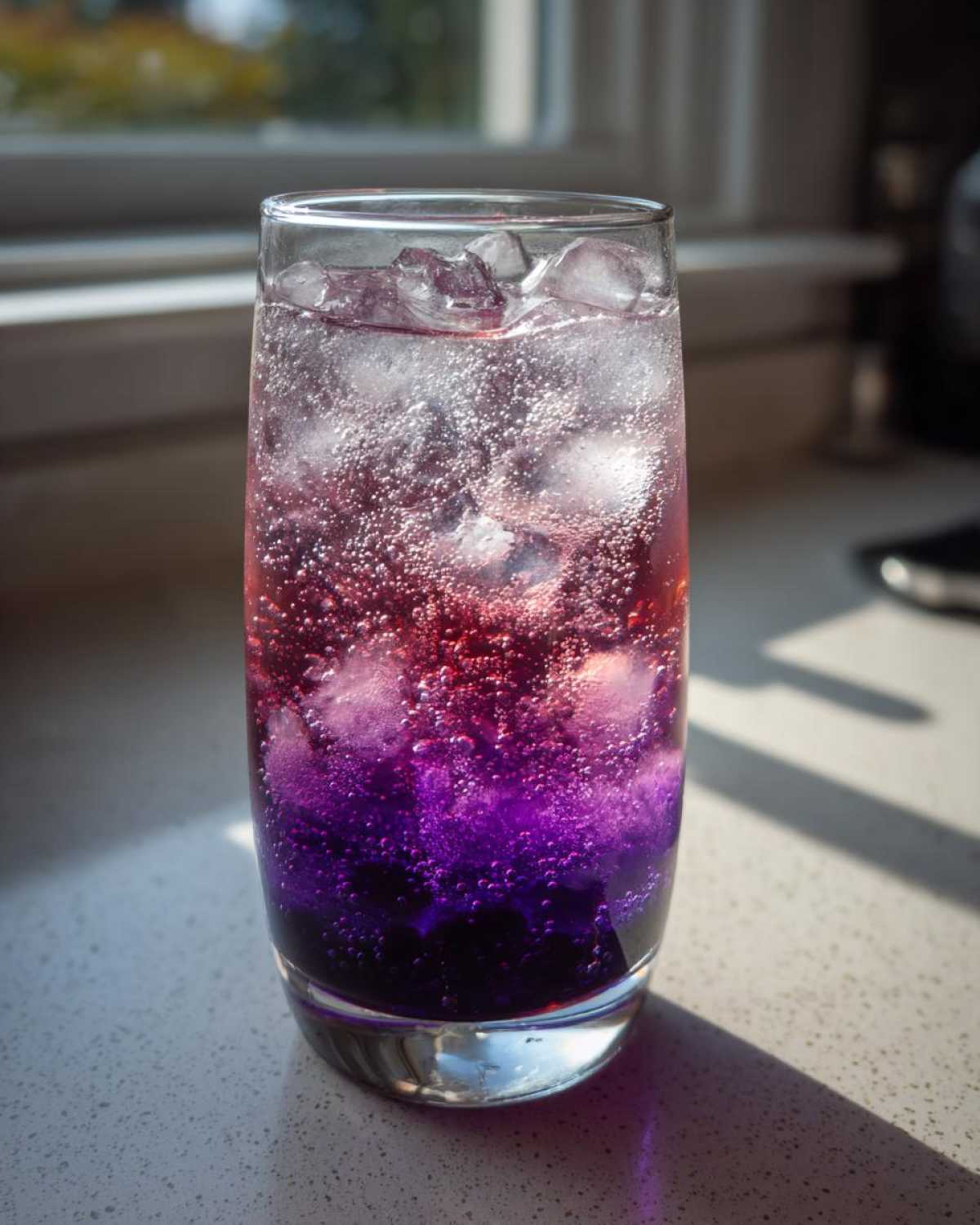 Close-up of a tall glass filled with a vibrant, layered Blueberry Jam Gin Spritz cocktail over ice cubes.