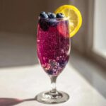A vibrant, bubbly Blueberry Lemosas Brunch Cocktail garnished with fresh blueberries and a lemon slice in a champagne flute.