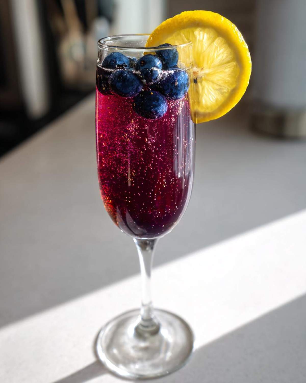 A vibrant, sparkling Blueberry Lemosas Brunch Cocktail garnished with fresh blueberries and a lemon slice.