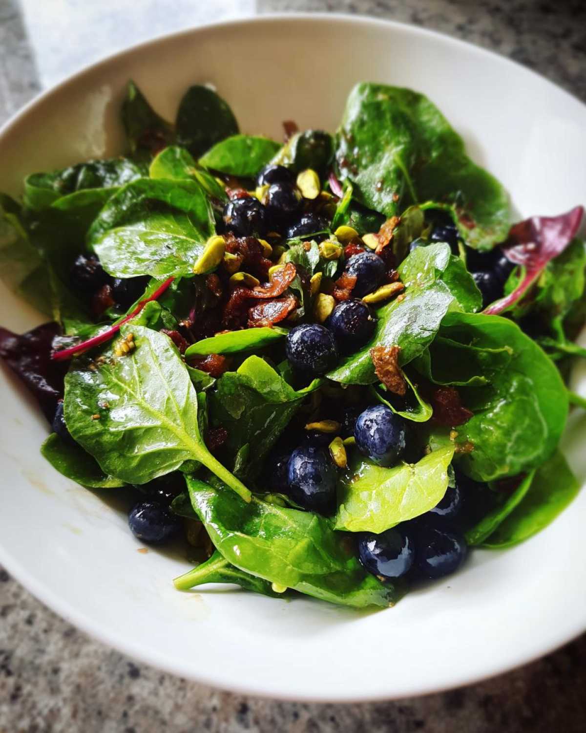 A vibrant close-up of a fresh Blueberry Pistachio Spring Salad featuring spinach, blueberries, and chopped pistachios.