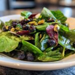Close-up of a fresh Blueberry Pistachio Spring Salad featuring spinach, blueberries, and bright green pistachios on a white plate.
