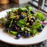Close-up of a fresh Blueberry Pistachio Spring Salad with mixed greens, bright blueberries, and chopped pistachios on a white plate.