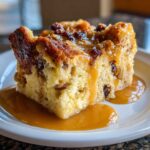 A close-up of a square slice of bread pudding with bourbon sauce generously drizzled over it.
