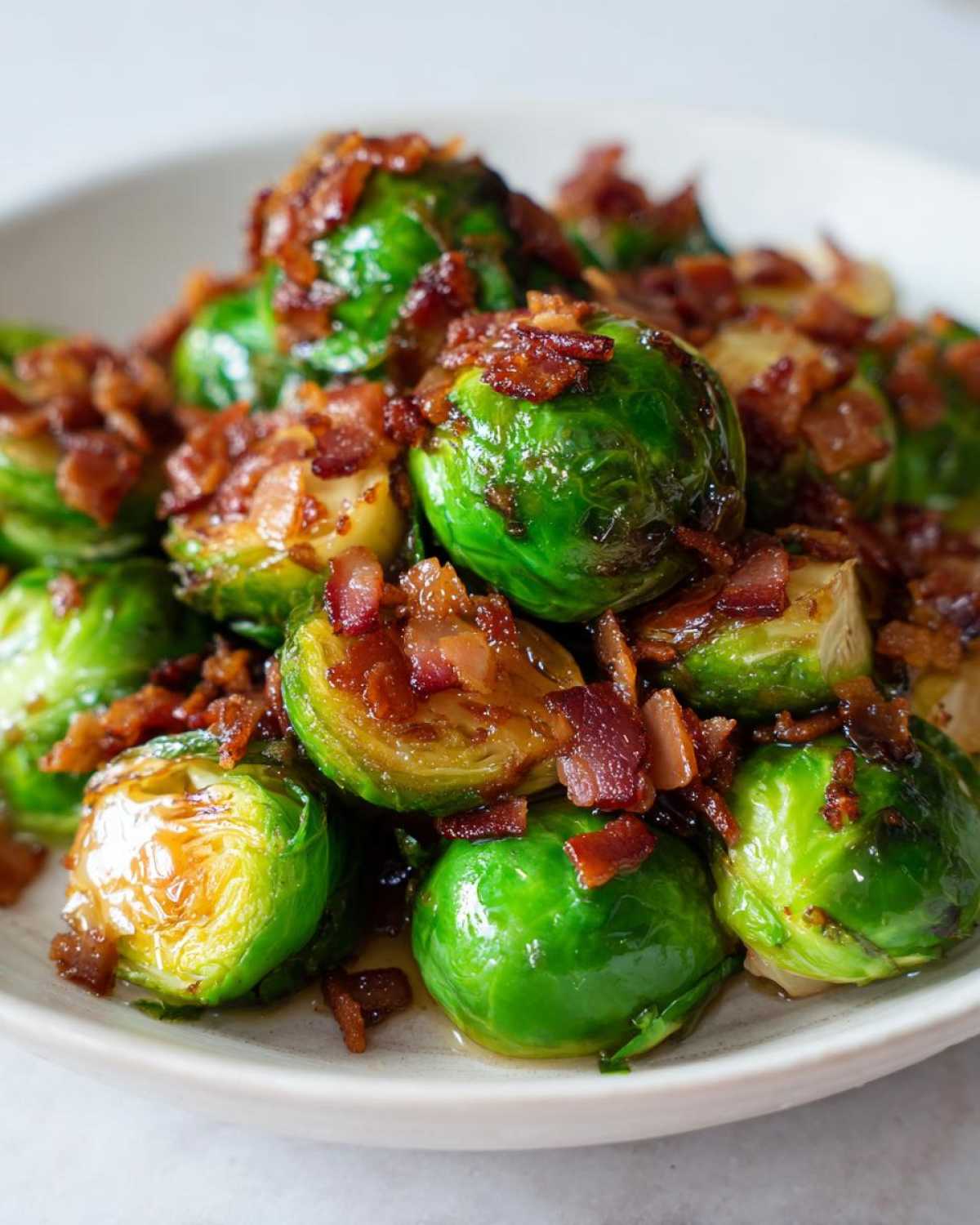 Close-up of vibrant green Brussels sprouts coated in a sweet glaze and topped with crispy bits of bacon.