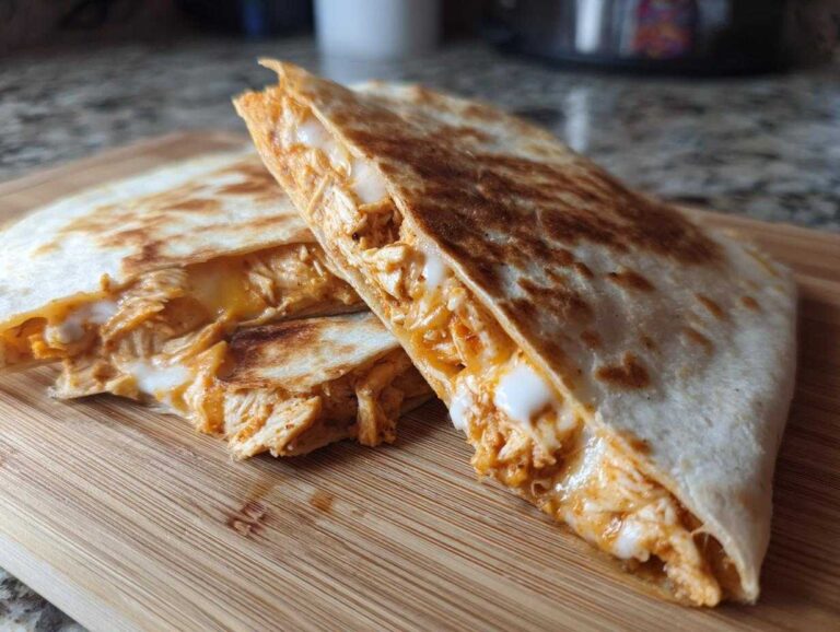 Two halves of a golden-brown buffalo chicken quesadilla showing melted cheese and shredded spicy chicken filling.
