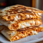 Close-up of stacked buffalo chicken quesadilla slices oozing with melted white cheese and spicy orange chicken filling.