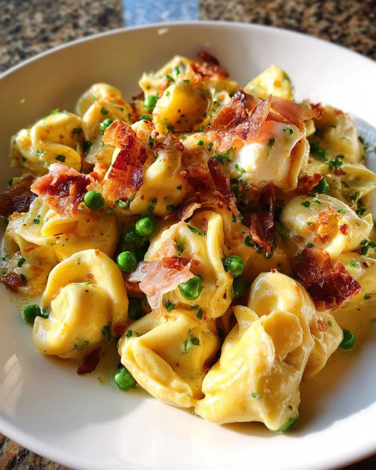 Close-up of a bowl of Burrata Pea and Prosciutto Tortellini coated in a creamy sauce and topped with crispy prosciutto.