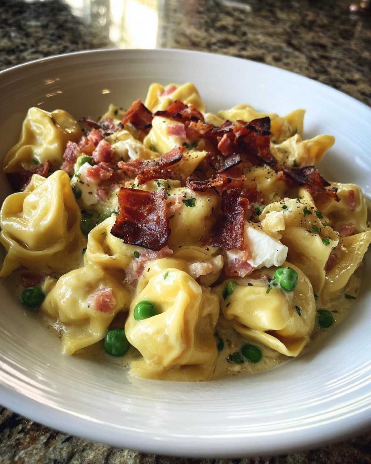A close-up of creamy Burrata Pea and Prosciutto Tortellini topped with crispy prosciutto pieces.