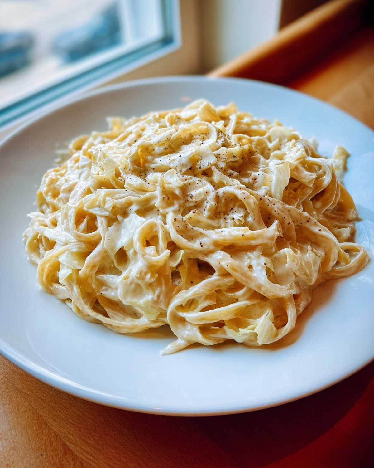 Close-up of a serving of Cabbage Alfredo Pasta coated in a rich, creamy sauce and topped with black pepper.