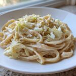 A close-up of creamy Cabbage Alfredo Pasta served on a white plate, featuring fettuccine noodles and wilted cabbage.