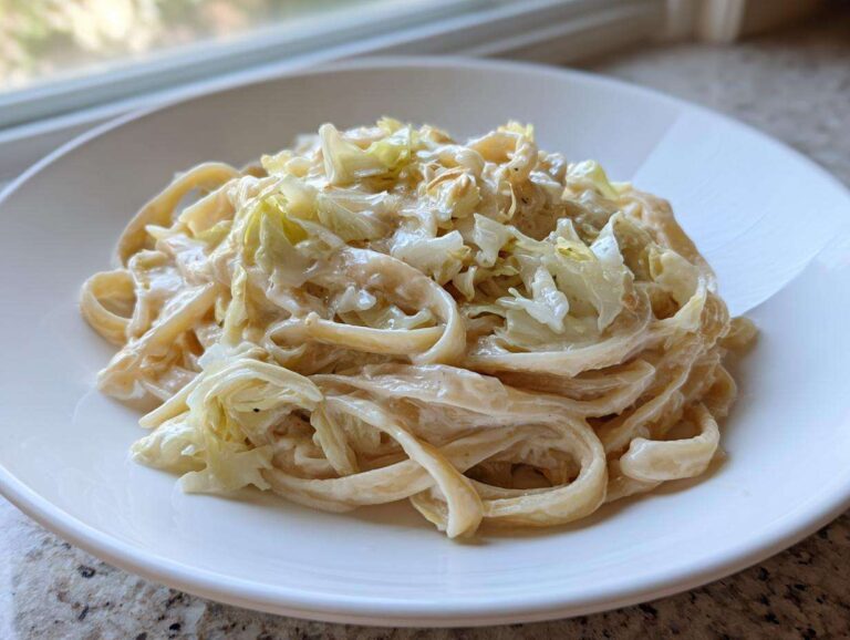 A close-up of creamy Cabbage Alfredo Pasta served on a white plate, featuring fettuccine noodles and wilted cabbage.