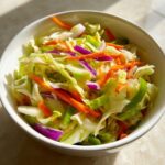 A vibrant bowl of Cabbage and Apple Crispy Slaw featuring shredded cabbage, carrots, red onion, and green pepper.