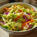 A vibrant bowl of Cabbage and Apple Crispy Slaw featuring shredded green cabbage, carrots, and red cabbage.