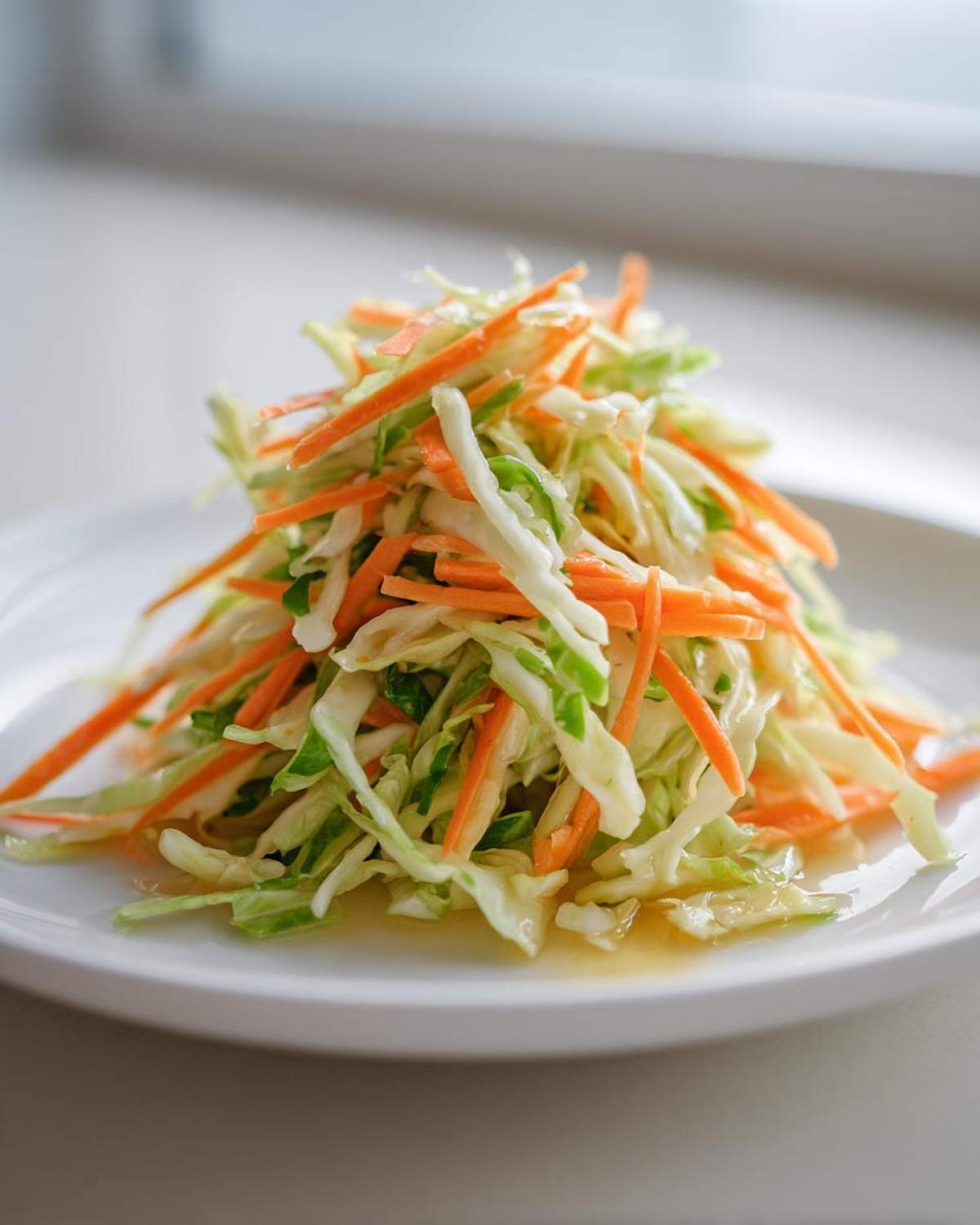 A mound of shredded cabbage and julienned carrots forming a vibrant Cabbage and Carrot Slaw No Mayo on a white plate.