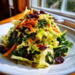 A mound of fresh Cabbage and Kale Power Salad topped with shredded carrots, pumpkin seeds, and dried cranberries.