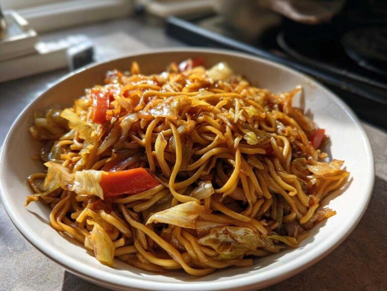A close-up of a bowl filled with savory Cabbage Noodle Stir Fry, featuring noodles, cabbage, and red peppers coated in sauce.